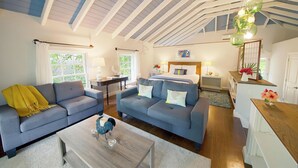 Un salon spacieux comprenant deux canapés, une table basse et un coin repas avec une table et des chaises en bois. De grandes fenêtres laissent entrer la lumière naturelle et offrent une vue sur la verdure environnante.