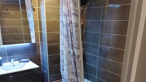Een moderne badkamer met een douchegordijn van marmer, een wastafel met spiegel en donkere betegelde muren.