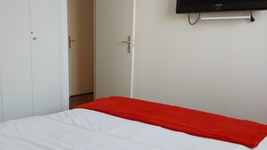 Een slaapkamer met een bed, een rode deken, een witte inbouwkast en een tv aan de muur.