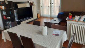 Een woonkamer met een televisie, een eettafel, stoelen, een bank en een boekenkast.