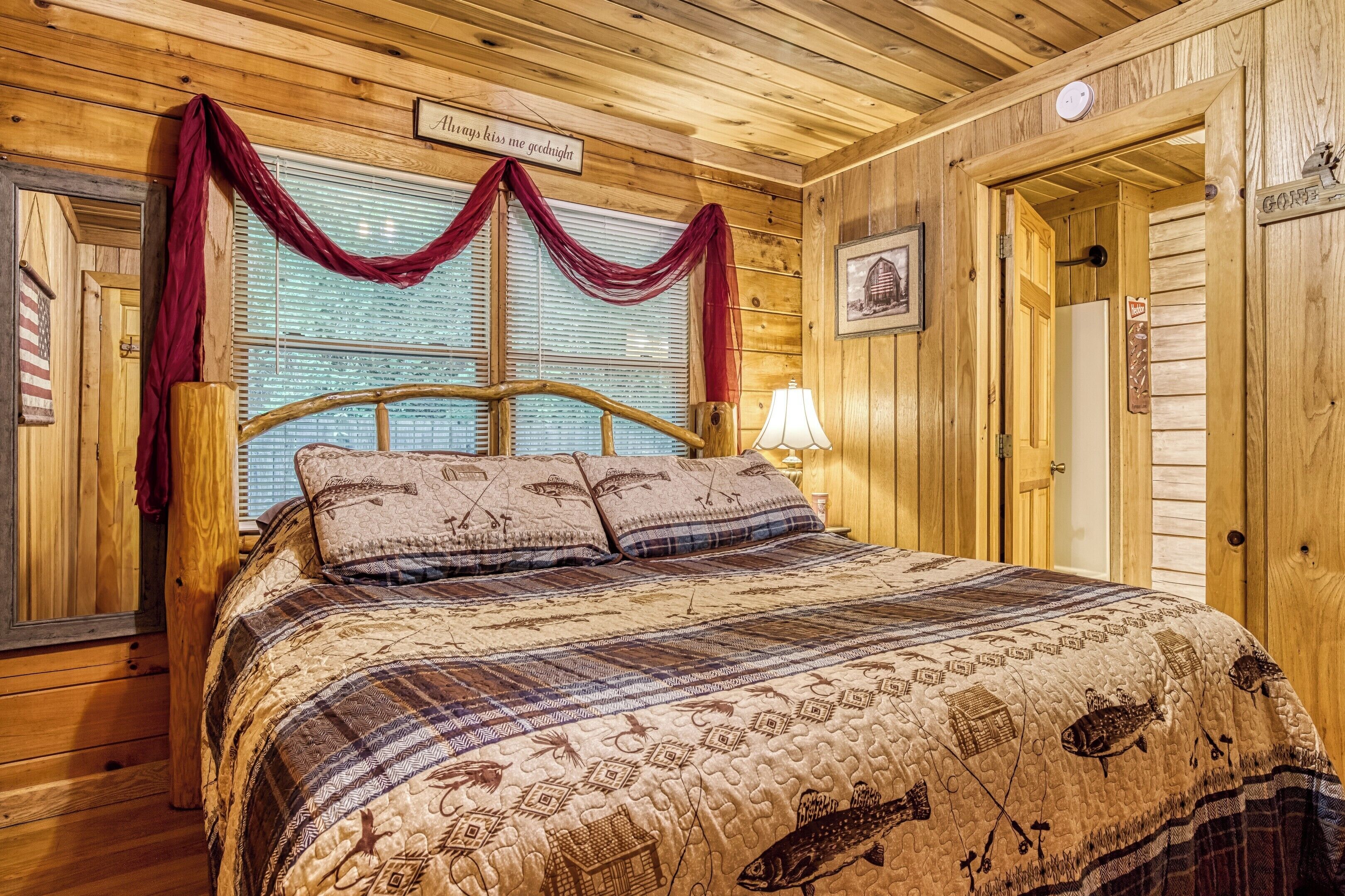 A wooden cabin-style bedroom with a large bed, a window with curtains, and a sign above the bed.