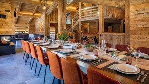 A wooden interior with a long dining table set for a meal, a fireplace, and a staircase. - Chalet Happyview - luxury holiday for 15 with pool & sauna - OVO Network (Le Grand-Bornand)
