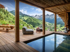 Une terrasse en bois avec une piscine, un espace salon extérieur et une vue panoramique sur les montagnes.