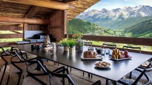 A wooden dining table with chairs, a view of mountains, and various food items. - Chalet Happyview - luxury holiday for 15 with pool & sauna - OVO Network (Le Grand-Bornand)