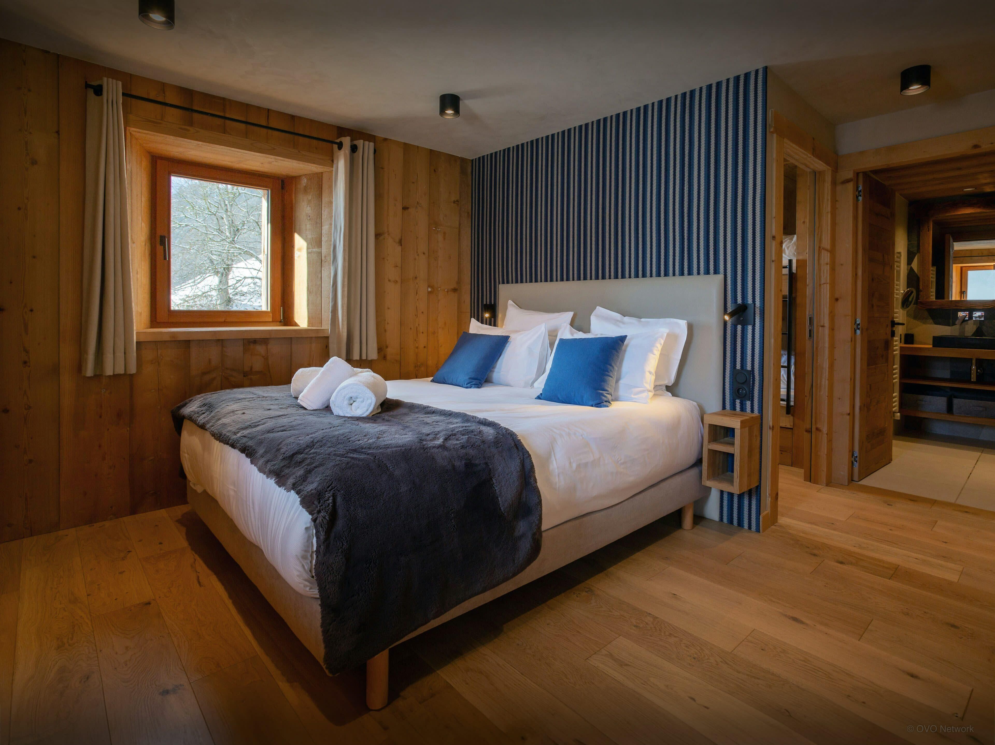 Ein Schlafzimmer mit Holzwänden, einem großen Bett, einem Fenster und Blick ins Freie.