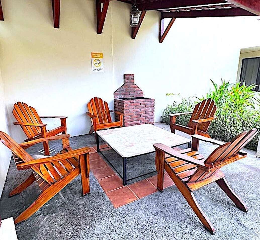 A patio with wooden Adirondack chairs, a brick barbecue grill, and a table.
