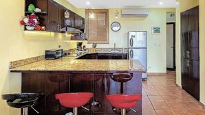 A kitchen with a central island, bar stools, a clock, and a refrigerator.