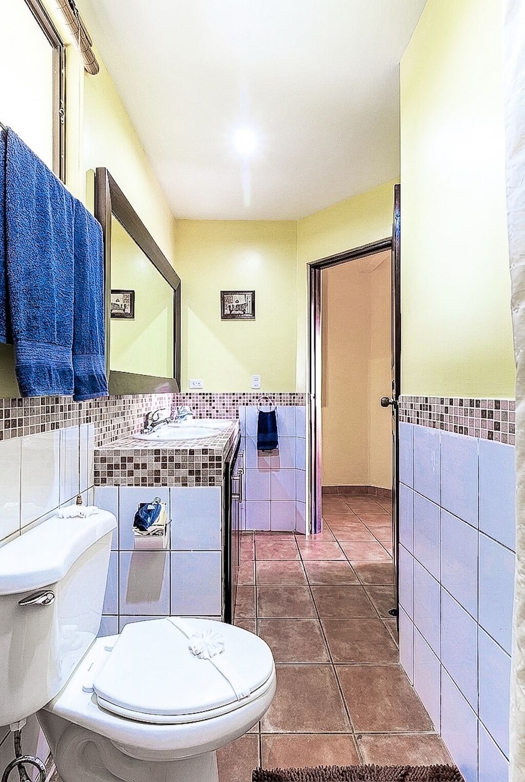 Ein Badezimmer mit Toilette, Waschbecken und Spiegel. Handtücher hängen an der Wand, und es gibt einen Duschbereich.