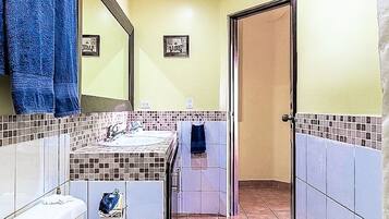 Ein Badezimmer mit Toilette, Waschbecken und Spiegel. Handtücher hängen an der Wand, und es gibt einen Duschbereich.