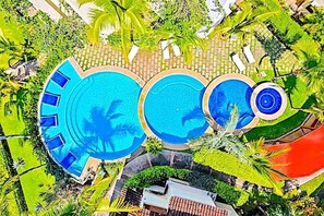 A large outdoor swimming pool with multiple levels, surrounded by lush greenery and palm trees. - COCO SUNSET HILLS  OCEAN VIEW CONDO, DIRECT RENTALS. COCO, COSTA RICA. (playas del Coco)