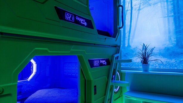 A futuristic room with two bunk beds, a digital oxygen meter, and a window with a view of trees. - Oxygen Hostel (Madrid)