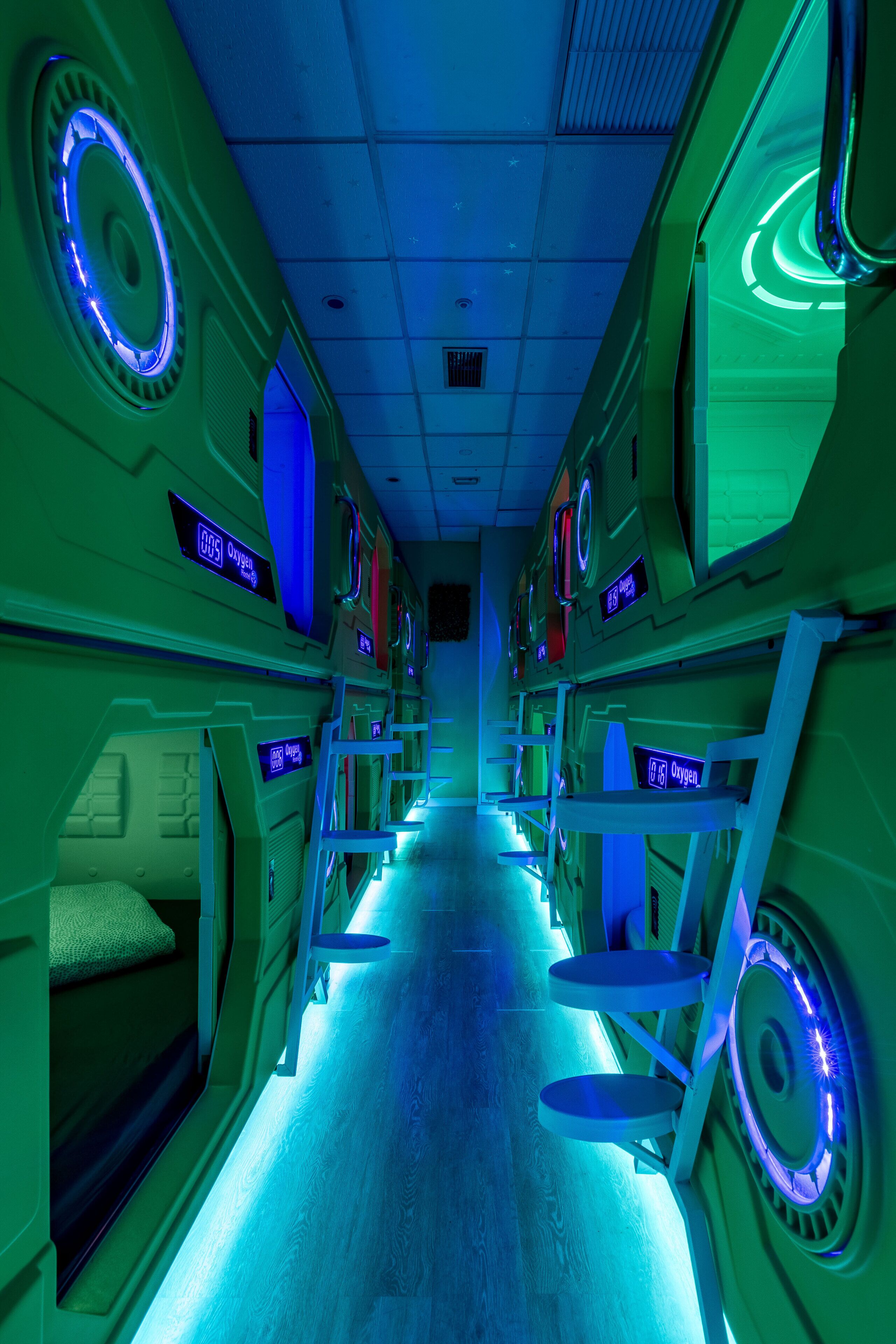 Un couloir futuriste, illuminé de néons, avec des lits superposés et des fenêtres rondes.