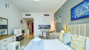 Habitació d'hotel moderna amb un llit gran, zona de seients amb un sofà i butaques, petita cuina i un bany visible a través d'una porta oberta.