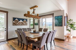 A dining area with a wooden table and upholstered chairs, a wooden ceiling light fixture, and framed artwork on the walls.