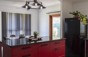 A modern kitchen with a black refrigerator, red cabinets, and a wooden dining table with chairs.
