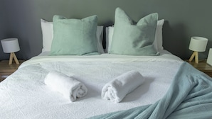 A neatly made bed with a white bedspread and two green pillows, a rolled white towel, and a white lamp on a wooden nightstand. - Pet Friendly, 2 Bedroom, Sleeps 4, 250m to Beach, Close to Cafes, Sunshine Coast (Marcoola)
