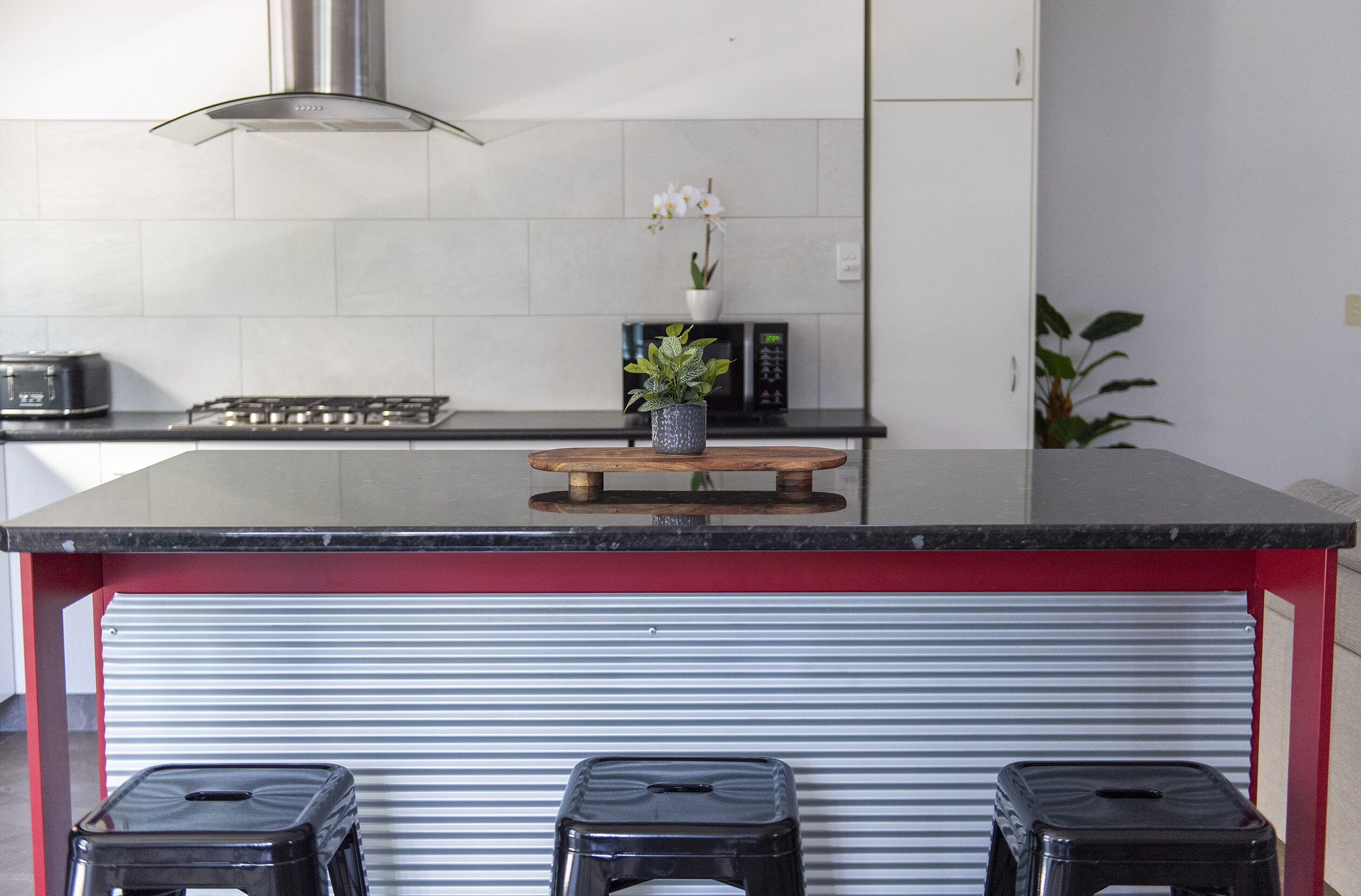 A kitchen with a black countertop, a stove, a microwave, a potted plant, and a red and white striped storage unit.