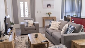 A modern living room with a grey sofa, a wooden coffee table, a grey armchair, and a TV on a wooden stand. - Pet Friendly, 2 Bedroom, Sleeps 4, 250m to Beach, Close to Cafes, Sunshine Coast (Marcoola)