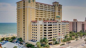 A multi-story hotel with a central courtyard, located near a beach with palm trees and a clear sky. - 15th floor 3 bedroom/2 bath condo with million dollar views! (Myrtle Beach)