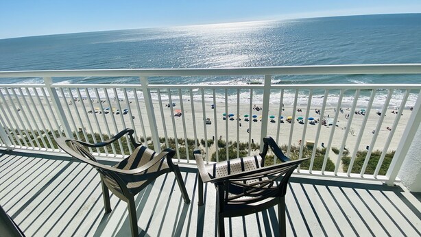 A balcony with two chairs overlooking a beach with umbrellas and people. - 15th floor 3 bedroom/2 bath condo with million dollar views! (Myrtle Beach)