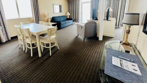 A hotel room with a dining table, chairs, a sofa, a small armchair, a desk with a lamp, and a TV. - 15th floor 3 bedroom/2 bath condo with million dollar views! (Myrtle Beach)