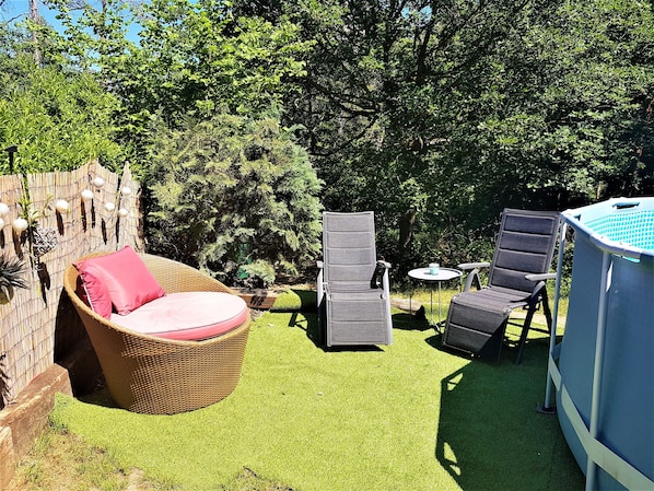 Ein Garten mit Korbstuhl, Tisch und Schwimmbecken.