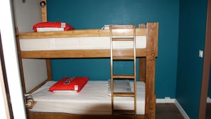 Un lit superposé avec une échelle, un oreiller rouge et un matelas blanc.