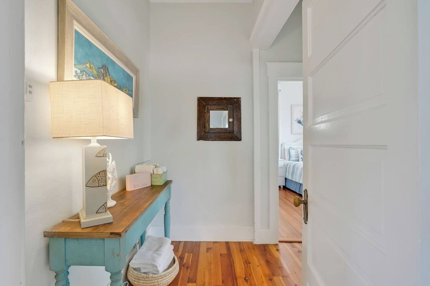 A hallway with a wooden bench, a lamp, a framed mirror, and a basket with towels.