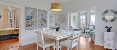 Un vaste espace de vie comprenant une table à manger, des chaises blanches et un luminaire suspendu.