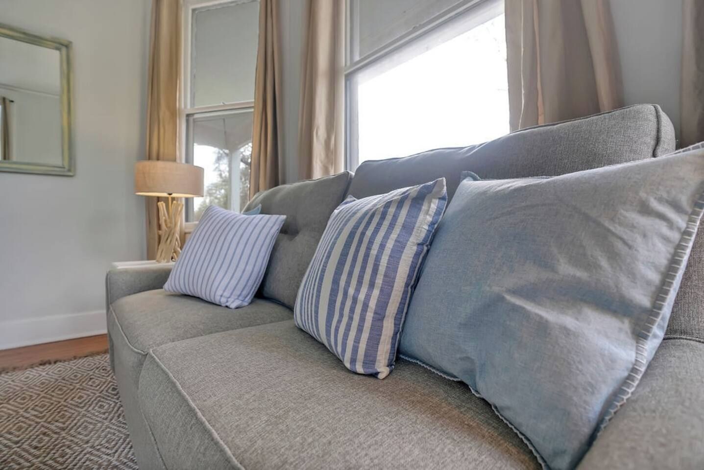 Un sofá gris con almohadones a rayas en una habitación con un tapete estampado, una lámpara y un espejo en la pared.