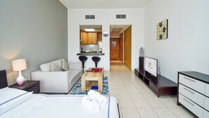Une chambre d’hôtel avec un lit, un bureau, une chaise, un canapé, une télévision et, au fond, une kitchenette.