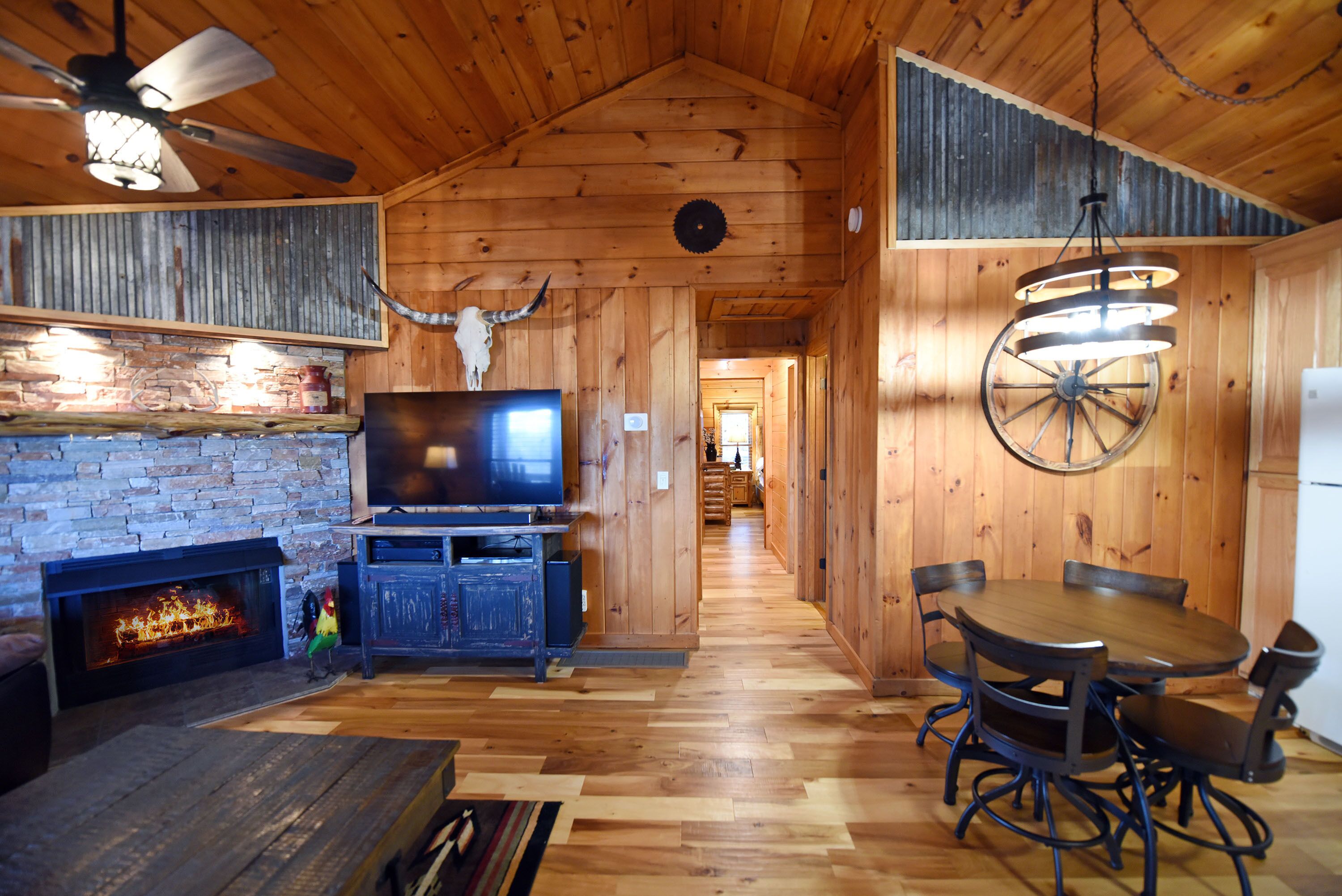 A wooden interior with a fireplace, a television, a dining table with chairs, and a ceiling fan.