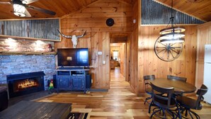 A wooden interior with a fireplace, a television, a dining table with chairs, and a ceiling fan.