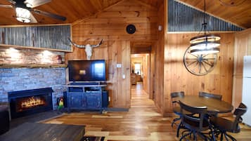 A wooden interior with a fireplace, a television, a dining table with chairs, and a ceiling fan.
