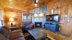 A cozy cabin interior with a stone fireplace, a television, and a sofa.