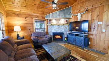 A cozy cabin interior with a stone fireplace, a television, and a sofa.