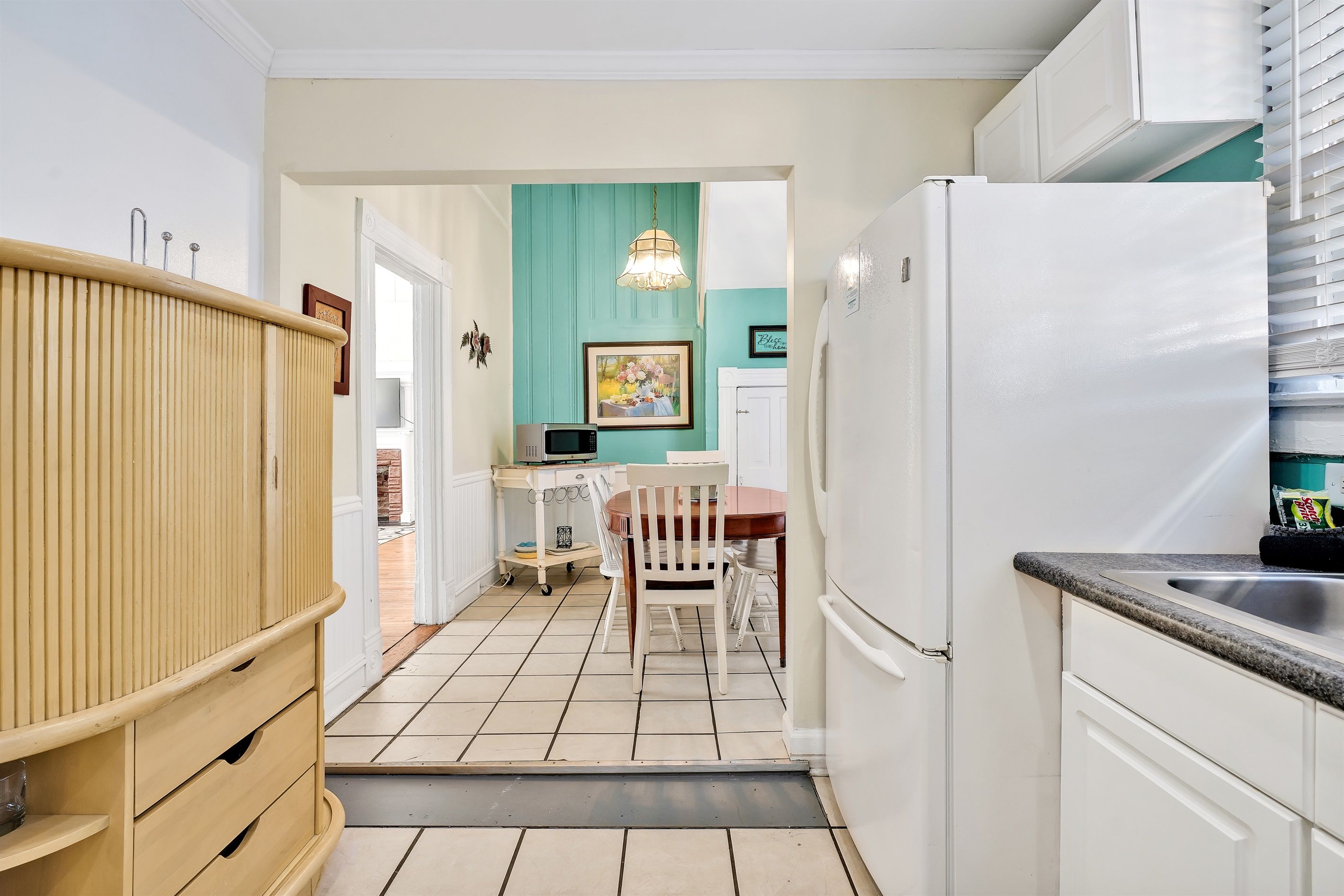 A compact kitchen with white cabinets, a white refrigerator, and a dining area with a wooden table and chairs.