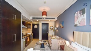 A modern hotel room with a large bed, a sofa, a dining area, and a kitchen.