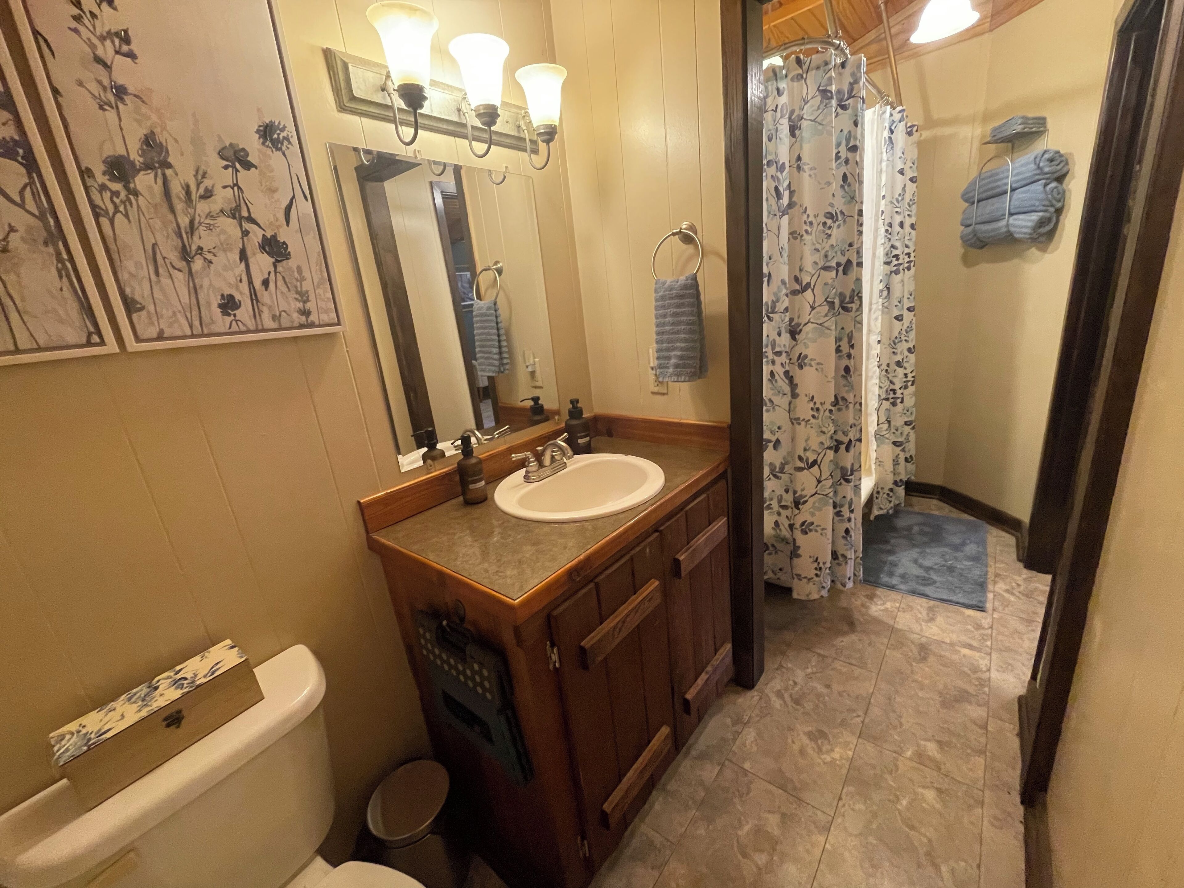 A bathroom with a wooden vanity, a white sink, a mirror, and a shower with floral curtains.
