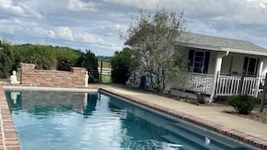 Ein rechteckiger Pool mit Backsteinbord, umgeben von einem Zaun und einem Haus mit Veranda.