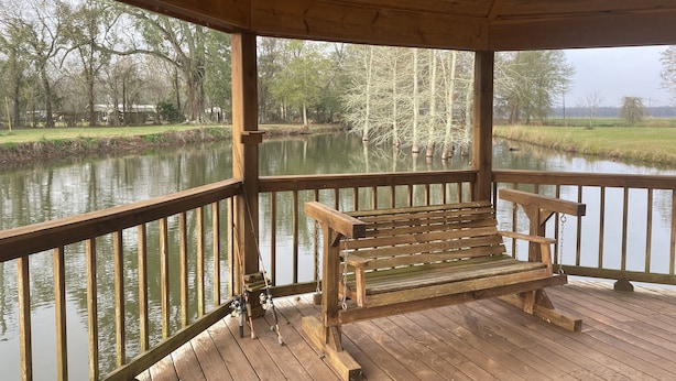 Eine Holzterrasse mit einer Bank, die auf ruhigem Wasser mit umliegenden Bäumen blickt.