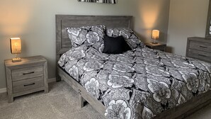 Ein Schlafzimmer mit einem Bett, zwei Nachttischen, einem Kopfteil, Wandkunst und einem Spiegel.