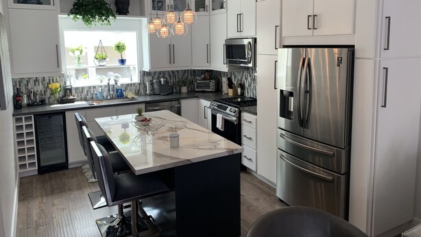 A modern kitchen with white cabinetry, stainless steel appliances, a central island with seating, and decorative plants.