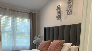 A modern bedroom with a grey upholstered headboard, white bedding, and decorative pillows.