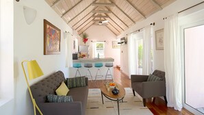 A spacious living area with a high ceiling, a sofa, two armchairs, a coffee table, and a kitchen in the background.