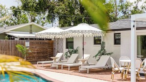 A pool area with lounge chairs and umbrellas, surrounded by a wooden fence and potted plants.