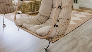 A room with a hanging chair and a sofa, both with beige cushions.
