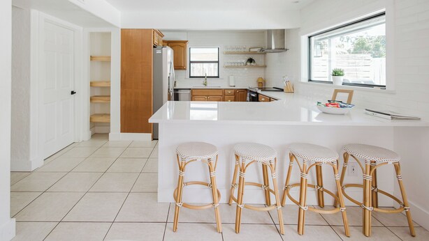 A modern kitchen with a large island, bar stools, wooden cabinets, and a window providing natural light.