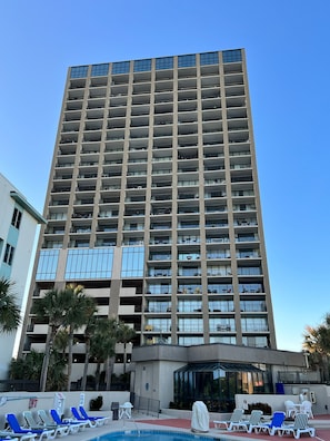 A high-rise hotel with multiple balconies, a swimming pool with lounge chairs, and palm trees. - Oceanfront Condo w/ Balcony - King Bed - Myrtle Beach - Pool (Myrtle Beach)