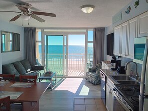 A spacious living room with a balcony overlooking the beach, a dining area, and a kitchen with a stove and sink. - Stunning Oceanfront Condo. Great resort. kitchen, W/D, 65" Roku tv, fast WIFI.. (Myrtle Beach)